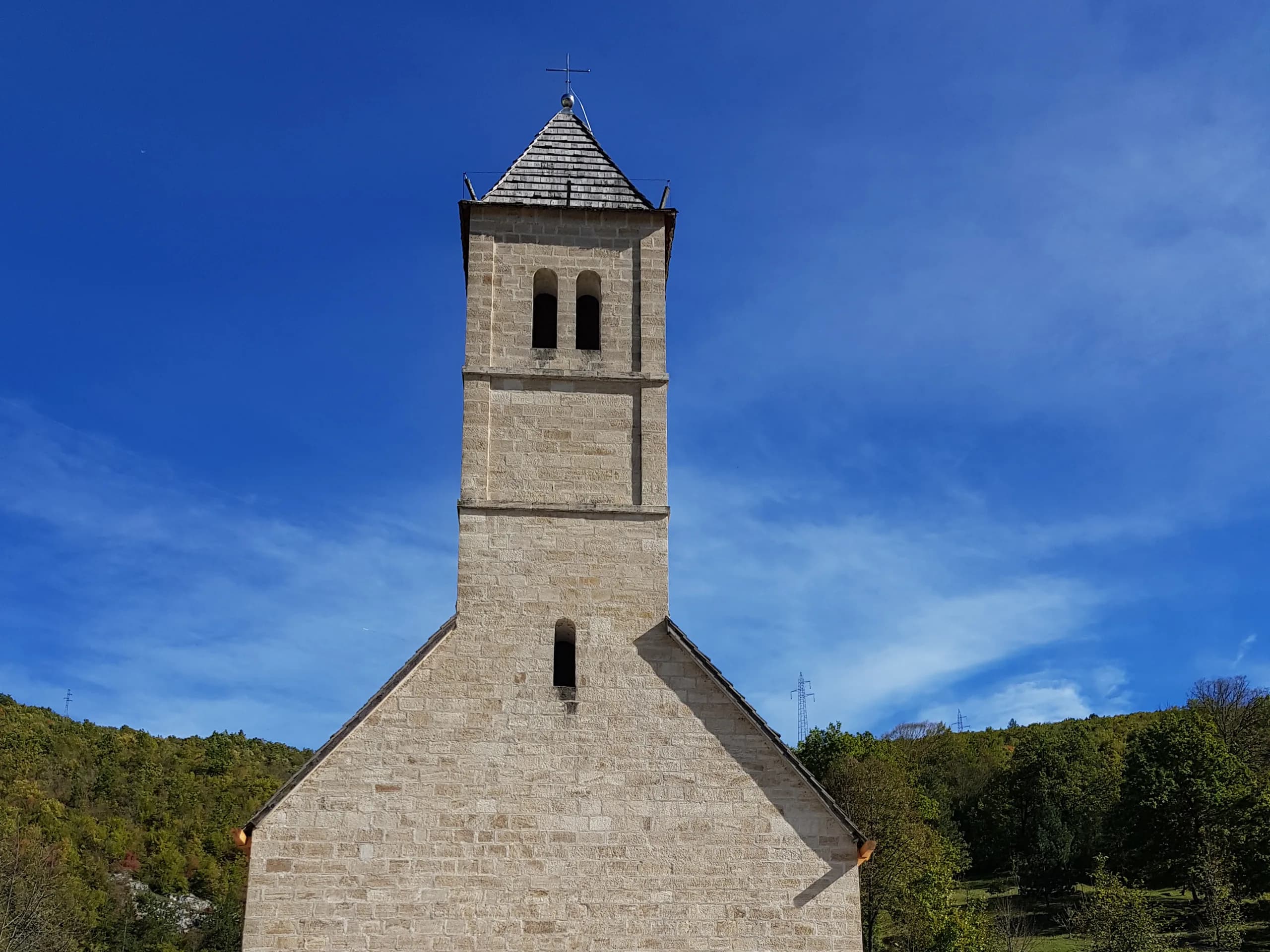 Glockenturm und Giebel der Steinkirche sv. Ivo in Podmilačje von vorn, unter blauem Himmel