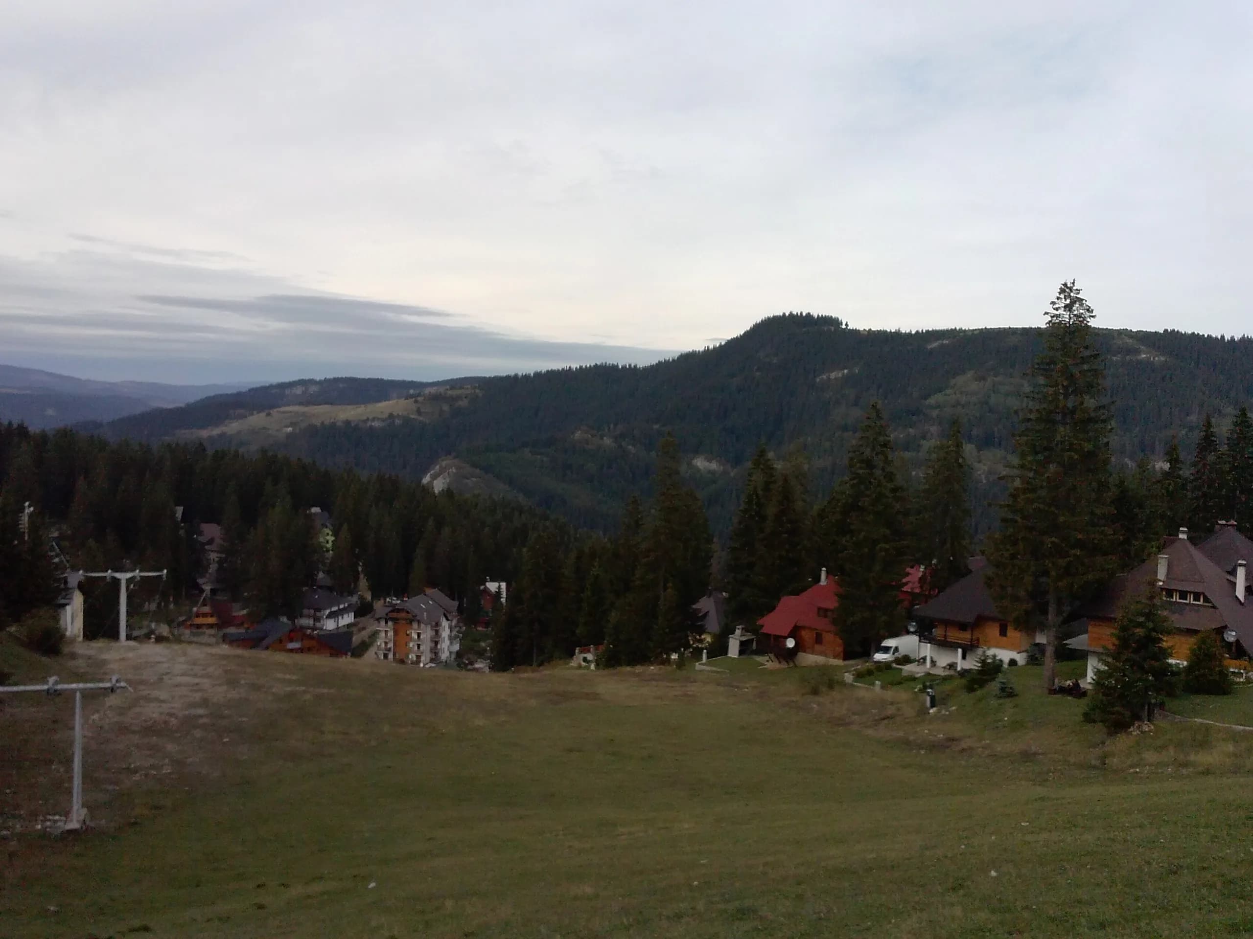 Grasbewachsene Skipiste in Babanovac mit Liftstützen, unten Hotels und Chalets, dahinter bewaldete Hügel