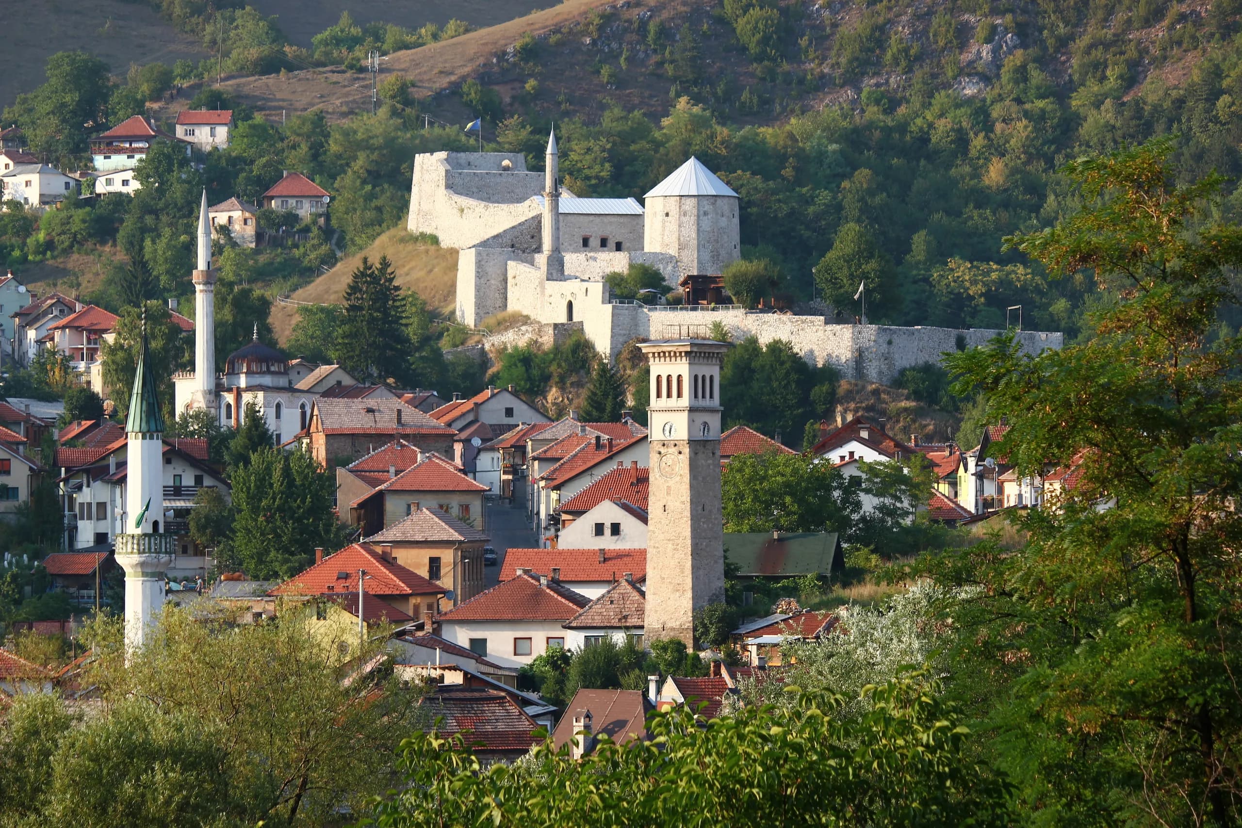 Blick über die Dächer von Travnik mit Uhrturm und Minaretten hinauf zur Festung am Hang